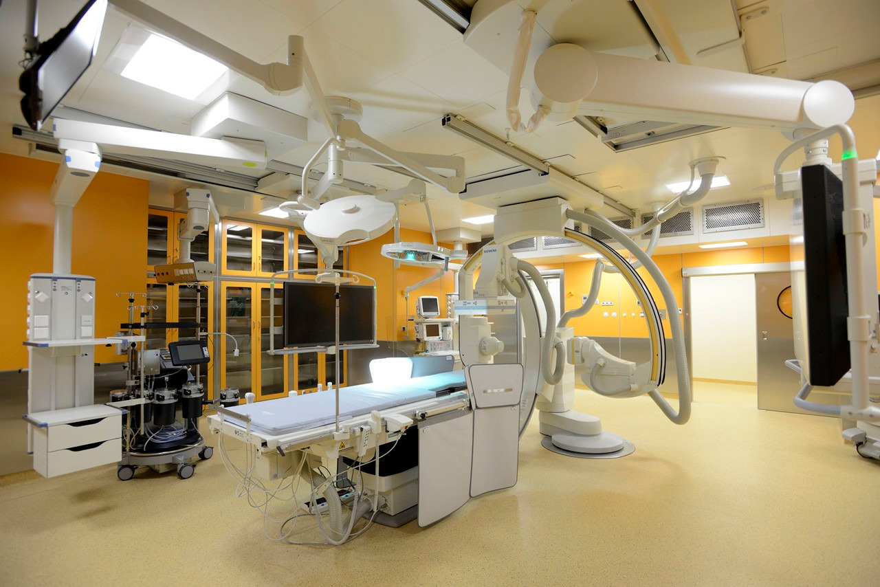 Jasna, przestronna sala operacyjna z nowoczesnym sprzętem medycznym, lampami sufitowymi i żółtymi ścianami, przygotowana do zabiegu.