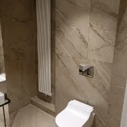 Nowoczesna łazienka z marmurowymi płytkami, wisząca toaleta i grzejnik drabinkowy.