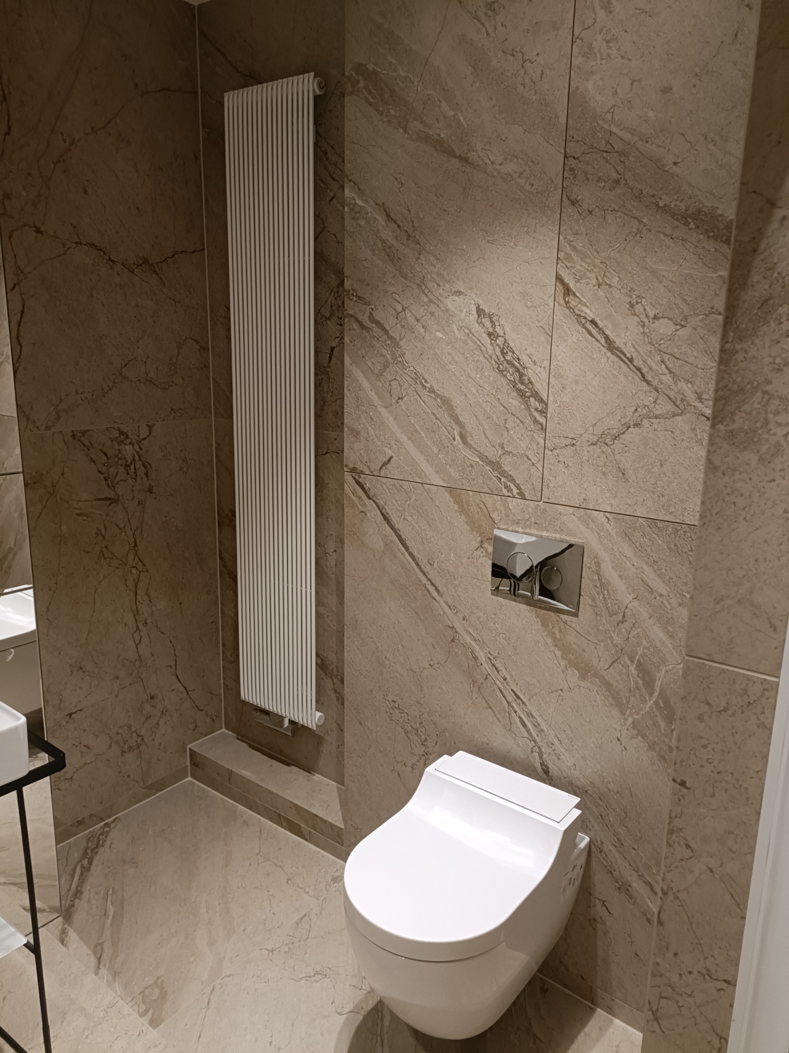 Nowoczesna łazienka z marmurowymi płytkami, wisząca toaleta i grzejnik drabinkowy.