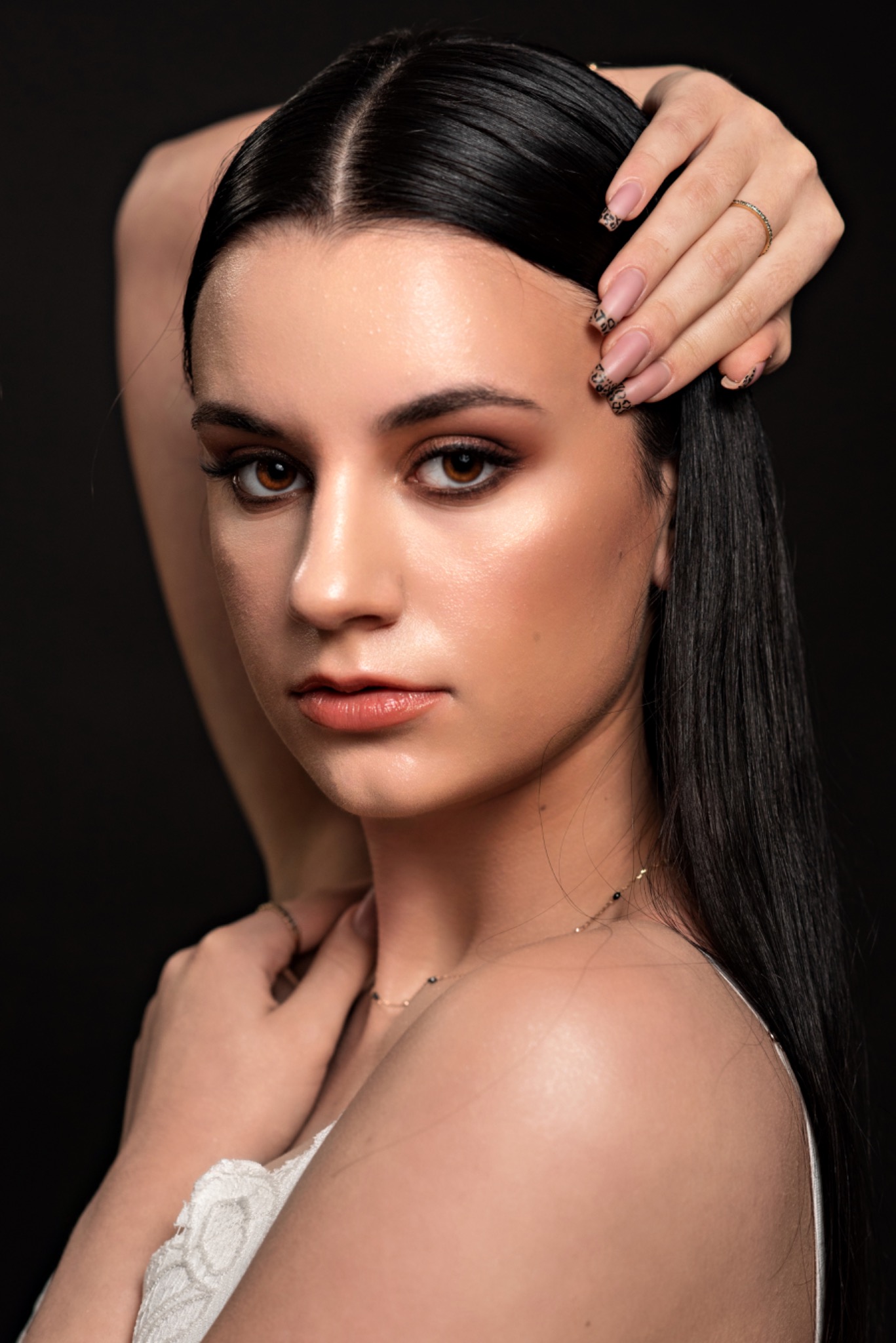 Portret kobiety z profesjonalnym makijażem oczu, błyszczącą cerą i modnym manicure w panterkę na paznokciach, pozującej na ciemnym tle.