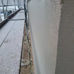 Świeżo otynkowana elewacja budynku w trakcie prac, widok z rusztowania pokrytego szronem.