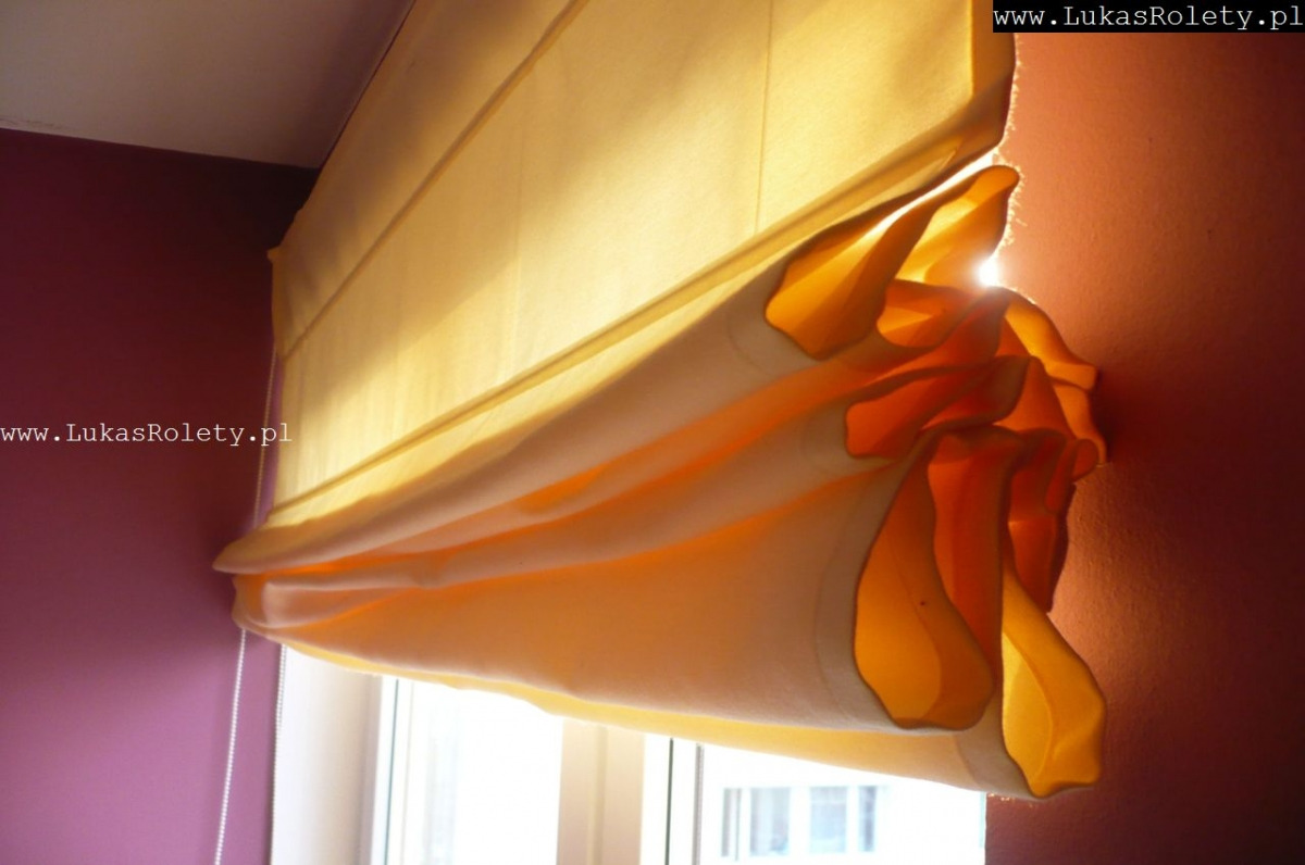 Żółta, materiałowa osłona okienna w stylu rzymskim, częściowo zwinięta, z widocznymi fałdami i delikatnym światłem słonecznym prześwitującym przez tkaninę, na tle ściany w kolorze fuksji...