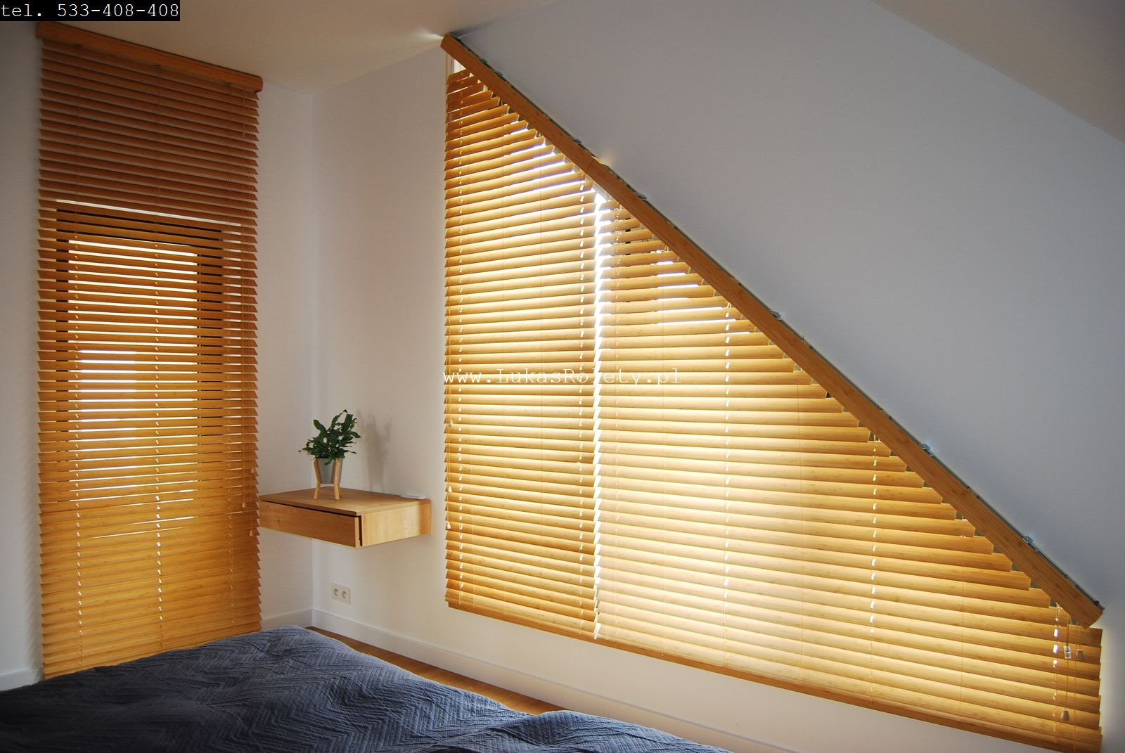 Jasne, drewniane żaluzje poziome zamontowane w oknie na poddaszu oraz w tradycyjnym oknie, obok wisząca szafka nocna z kwiatkiem, widok na fragment łóżka z szarą narzutą.