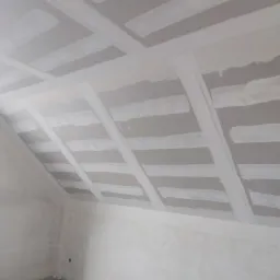 Poddasze w trakcie ocieplania z widoczną konstrukcją z płyt kartonowo-gipsowych i częściowo nałożonymi warstwami szpachli.