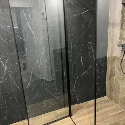 Nowoczesna kabina prysznicowa z czarnymi płytkami imitującymi marmur i drewnopodobnymi płytkami podłogowymi ułożonymi w jodełkę na ścianie.