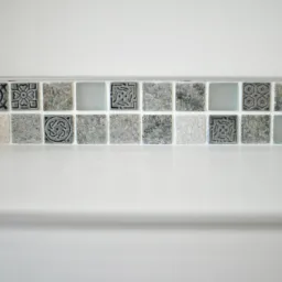 Rząd mozaiki z płytek o zróżnicowanych wzorach i fakturach, ułożony nad białą, gładką powierzchnią blatu lub wanny, z widoczną fugą w kolorze zbliżonym do bieli.
