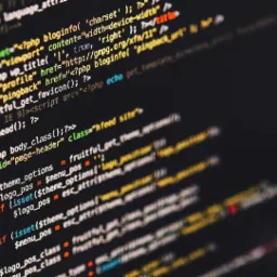 Ekran monitora z wyświetlonym kodem PHP w różnych kolorach, widoczne fragmenty funkcji, zmiennych i atrybutów, ciemne tło.