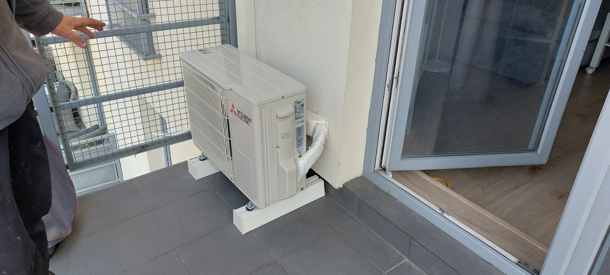 Zewnętrzna jednostka klimatyzacji Mitsubishi Electric zamontowana na balkonie, widoczna część sylwetki instalatora.