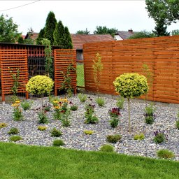 Blossom Garden - Nowoczesny ogród z drewnianym ażurowym i pełnym płotem, kulistymi drzewkami, rabatą z kamyków i kolorowymi kwiatami.