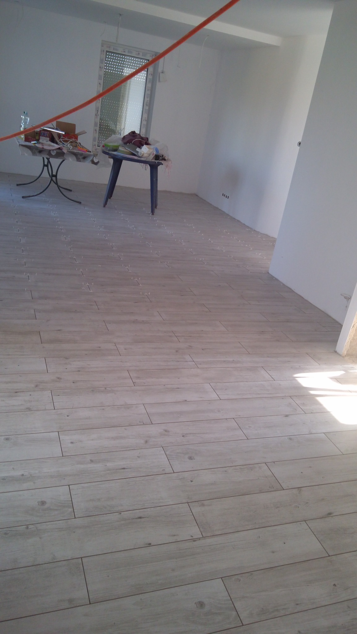 Układanie paneli podłogowych imitujących drewno w jasnym, nowo wykończonym pomieszczeniu z widocznymi krzyżykami dystansowymi między panelami, dwa stoliki z narzędziami i materiałami budowlanymi...