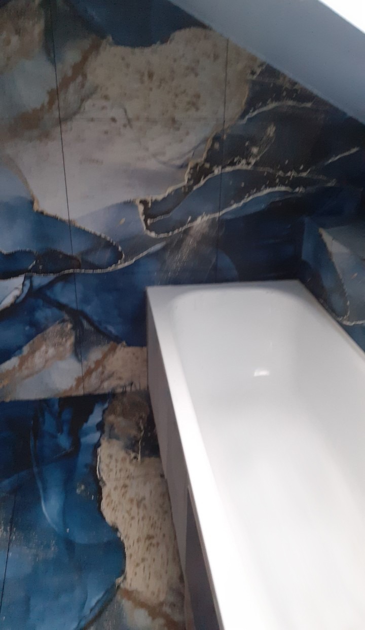 Biała wanna narożna pod skosem, otoczona ścianami z niebiesko-złotymi wzorami przypominającymi marmur lub płynne abstrakcje.