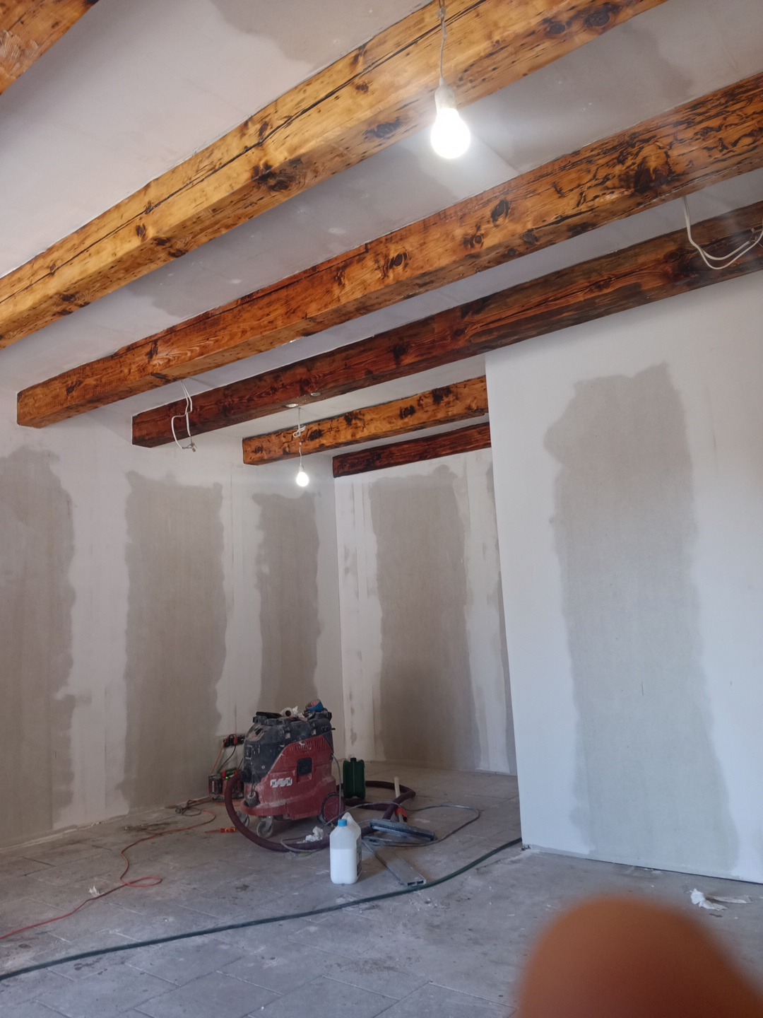 Wnętrze w Twardogórze po szpachlowaniu, z widocznymi drewnianymi belkami stropowymi i sprzętem budowlanym, gotowe do dalszych prac wykończeniowych.