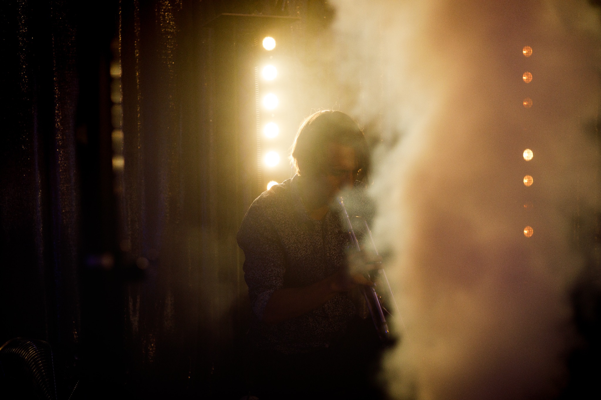 Sylwetka muzyka grającego na instrumencie dętym na scenie w oparach dymu i podświetleniu reflektorami punktowymi.