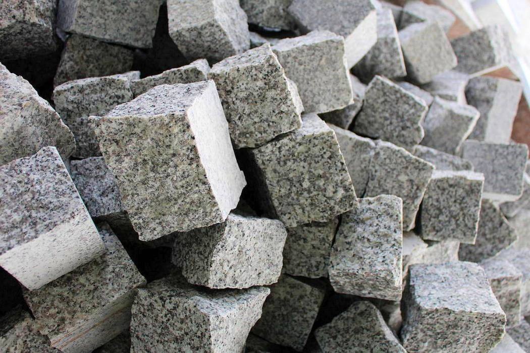 Stos kostek granitowych o szorstkiej fakturze, przygotowanych do ułożenia na tarasie lub podjeździe, z widocznymi śladami obróbki kamieniarskiej.