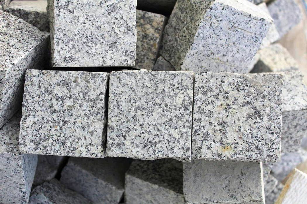 Stos szarych, kwadratowych kostek brukowych z granitu o nieregularnej fakturze, ułożonych blisko siebie.