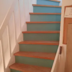 Schody z drewnianymi stopniami i pomalowanymi na niebiesko podstopnicami oraz białą barierką, widok z dołu.