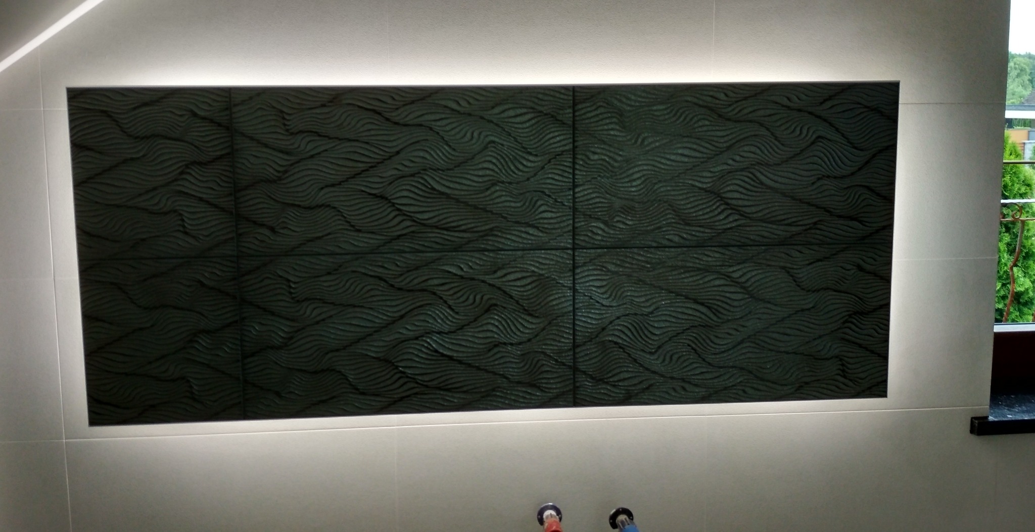 Panel ścienny z ciemnych płytek z falistym wzorem, podświetlony listwą LED, w jasnej łazience.