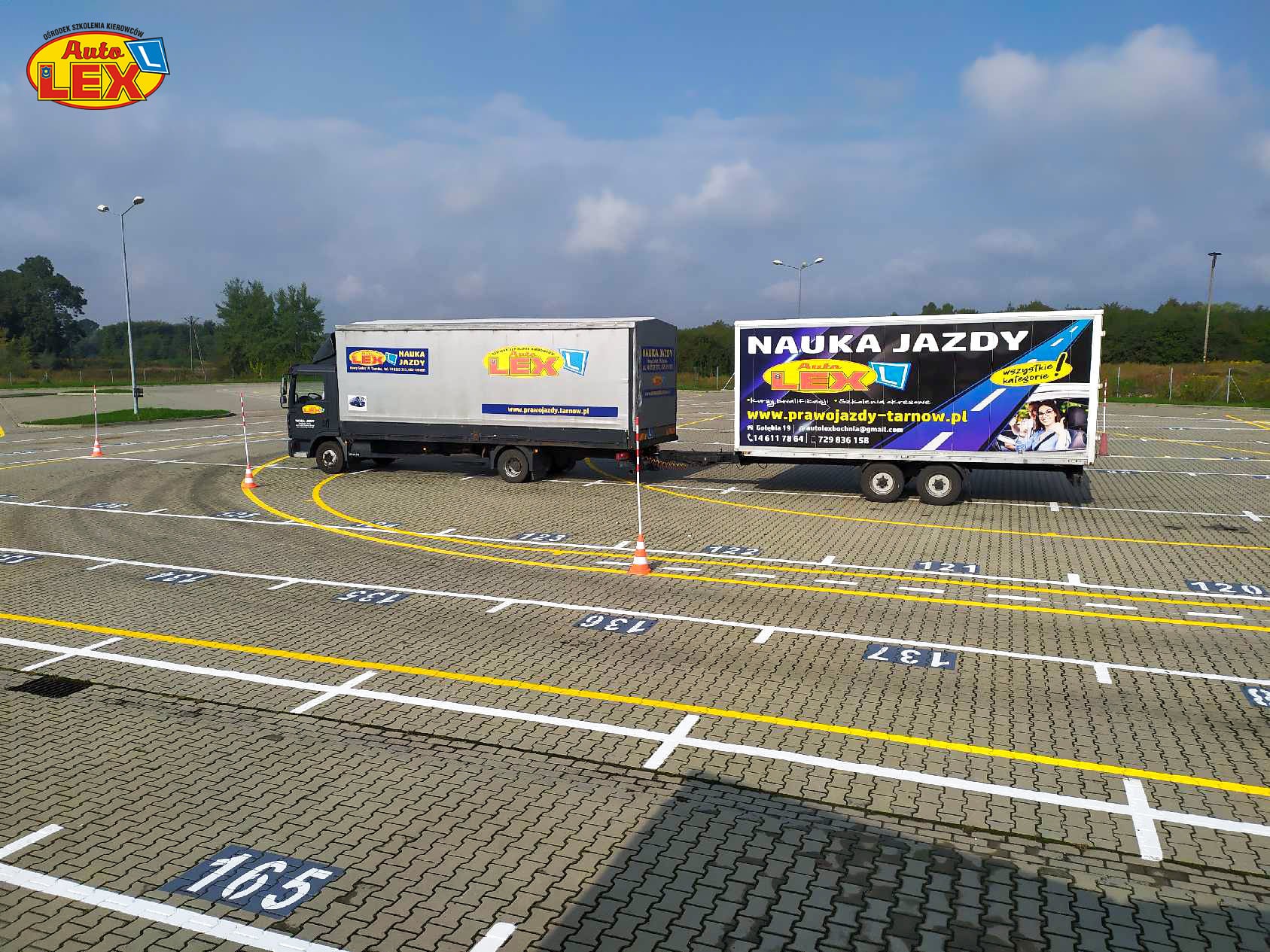 Dwa samochody ciężarowe z przyczepami z logo ośrodka szkolenia kierowców na placu manewrowym z oznaczonymi stanowiskami i torem do egzaminu na prawo jazdy kategorii C+E.