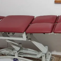 Rozłożony, regulowany stół do terapii manualnej z bordową tapicerką i białym stelażem, widoczny z boku, z zagłówkiem i dodatkowym podnóżkiem.