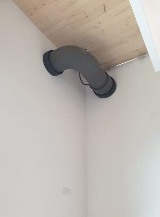 Szary kanał wentylacyjny w kształcie litery U, przymocowany do białej ściany i drewnianego sufitu pod kątem.