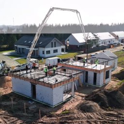 CONCRETEX GROUP SPÓŁKA Z OGRANICZONĄ ODPOWIEDZIALNOŚCIĄ - Wylewanie betonu na strop domu murowanego z betoniarki z długim ramieniem, widoczni pracownicy w kamizelkach odblaskowych, w tle zabudowa jednorodzinna.