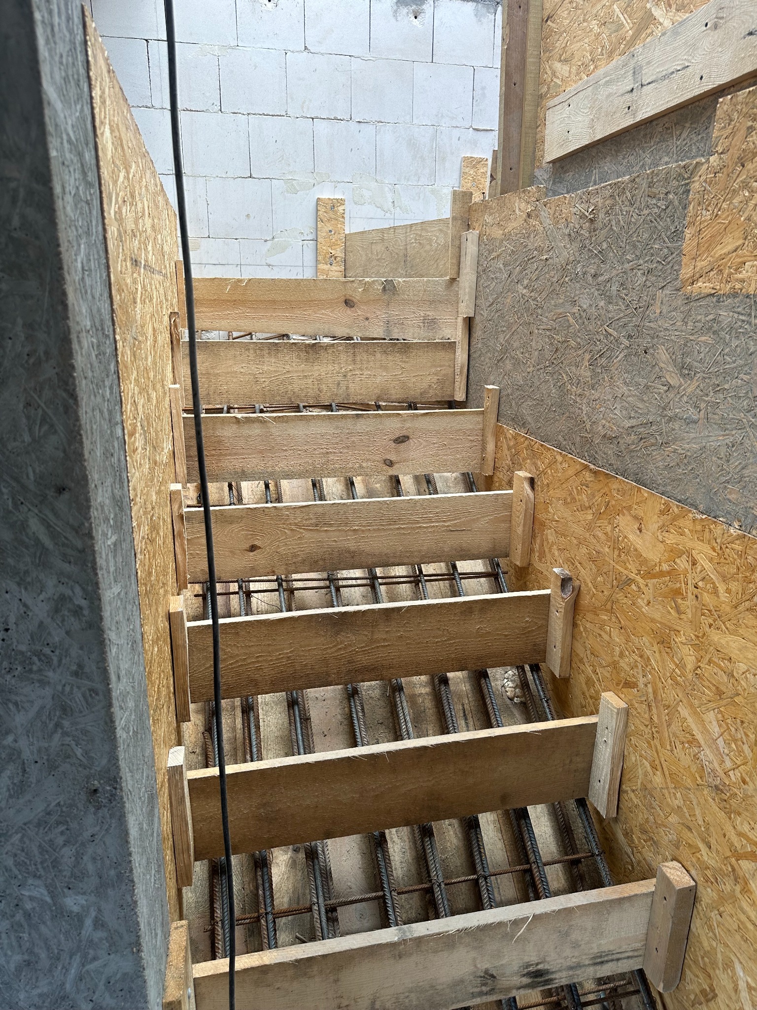 Szalunek schodów z drewnianych desek i zbrojenia stalowego, widok z góry na placu budowy, ściana z bloczków betonu komórkowego w tle.