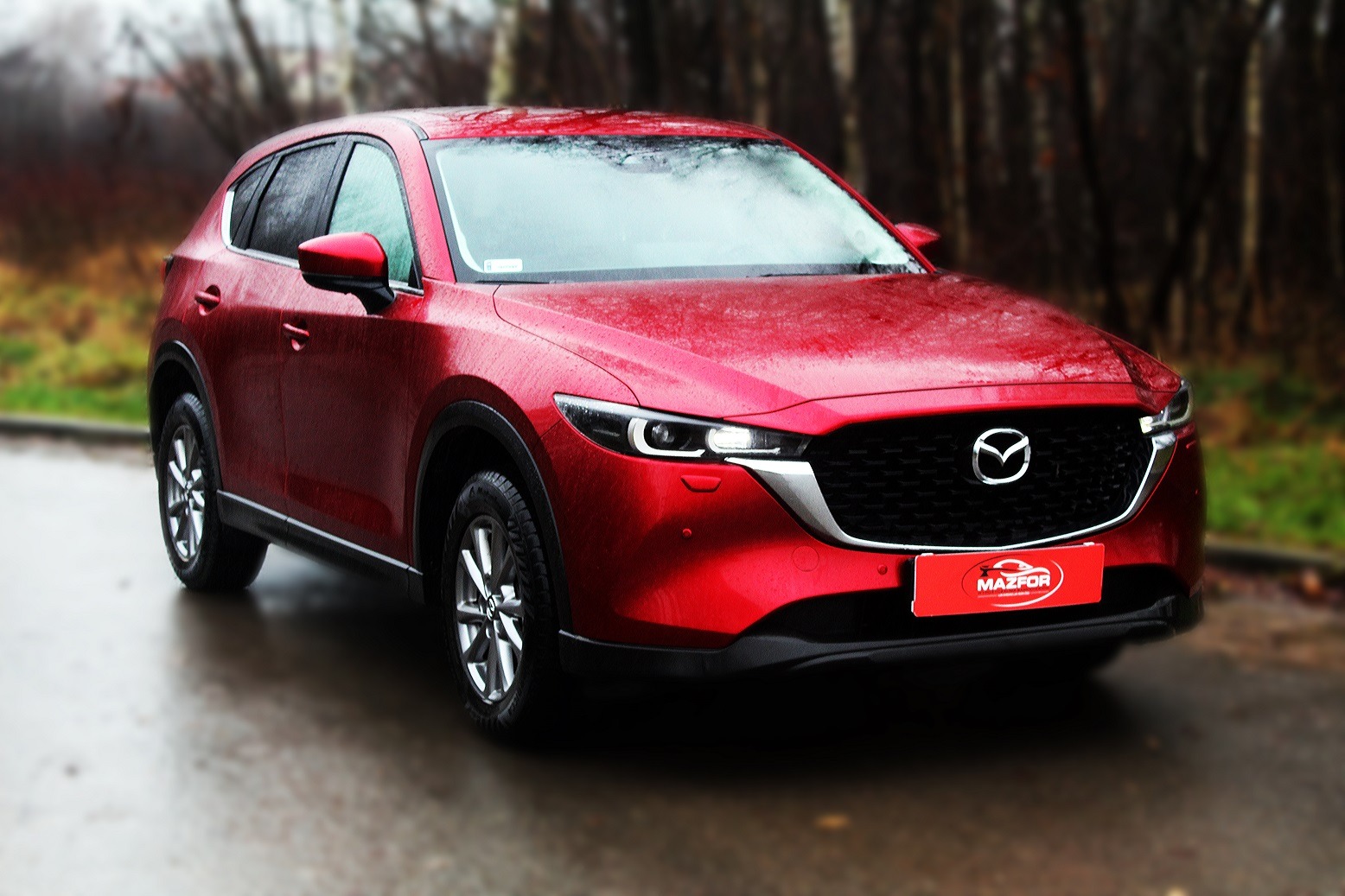 Czerwony samochód Mazda CX-5 na mokrej nawierzchni, z widocznym logo firmy Mazfor na tabliczce z przodu.