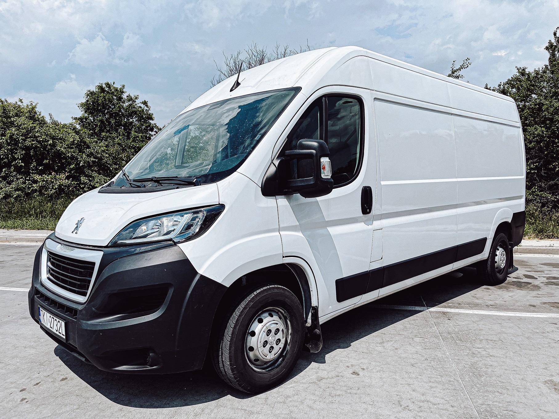Biały samochód dostawczy Peugeot z widoczną tablicą rejestracyjną, zaparkowany na betonowym placu w słoneczny dzień.