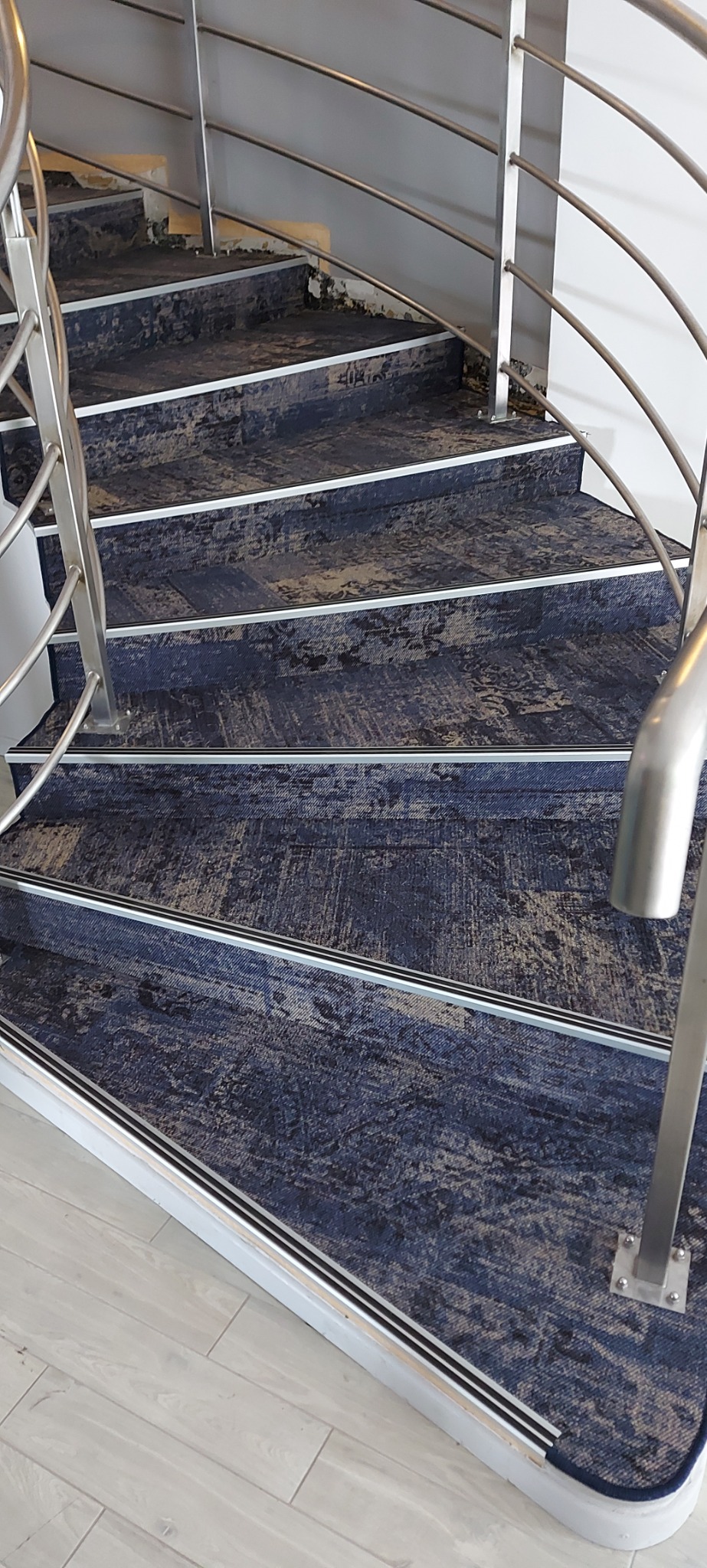 Schody wyłożone dywanem w odcieniach granatu i beżu, z metalowymi poręczami i listwami przypodłogowymi.