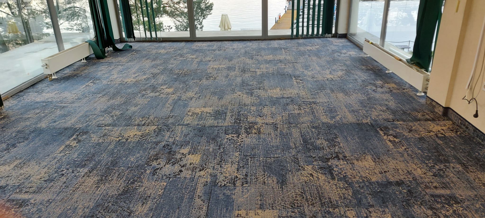 Nowoczesna, wzorzysta wykładzina w odcieniach szarości i beżu w przestronnym pomieszczeniu z dużymi oknami i widokiem na wodę.