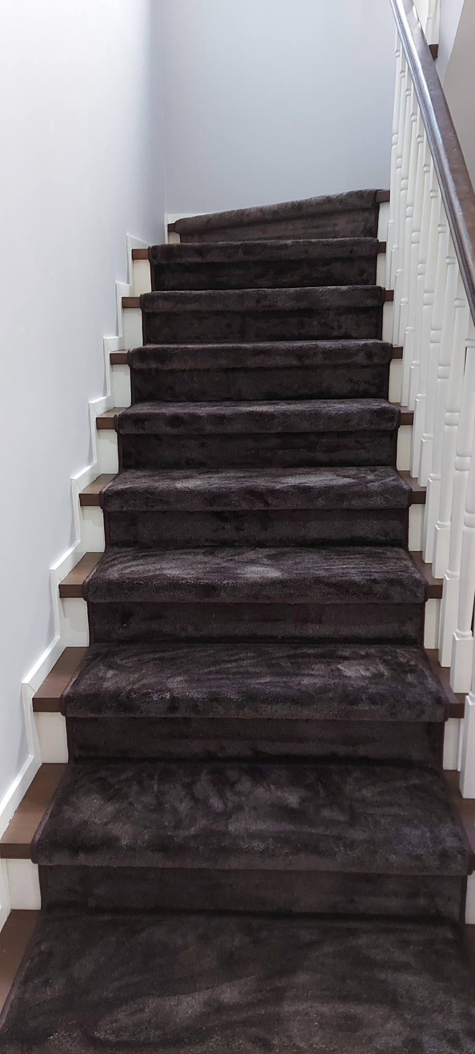 Schody w domu pokryte brązową wykładziną dywanową, białe listwy przypodłogowe i drewniane stopnice.