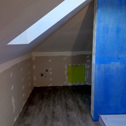 Usługi Remontowo-Budowlane Arkadiusz Witek - Poddasze w trakcie adaptacji na łazienkę: widoczne płyty karton-gips na ścianach z miejscowymi szpachlowaniami, fragment niebieskiej hydroizolacji oraz ułożone panele podłogowe imitujące drewno.