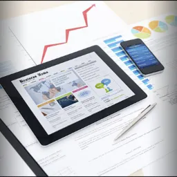 Tablet z artykułem o finansowaniu dla firm, obok smartfon z wykresami i długopis na dokumentach, widoczny fragment filiżanki kawy.