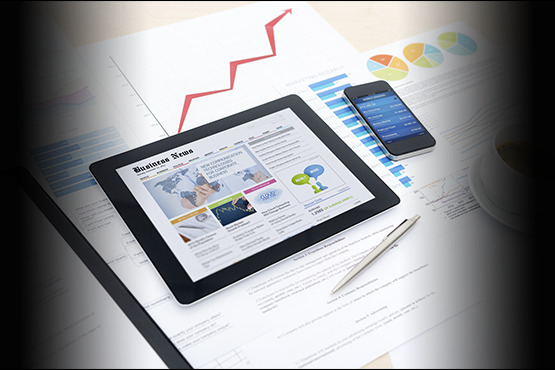 Tablet z artykułem o finansowaniu dla firm, obok smartfon z wykresami i długopis na dokumentach, widoczny fragment filiżanki kawy.