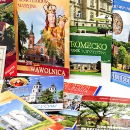 Stos różnych publikacji drukowanych, w tym przewodniki turystyczne i książki o tematyce religijnej, z widocznymi zdjęciami kościołów i sanktuariów, ustawionych na białym tle.