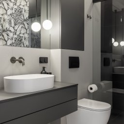 IWONA MAŁGORZATA CHMIELEWSKA PROFIT LINE - Nowoczesna łazienka w szarościach z białą umywalką nablatową i toaletą, wzorzysta tapeta w tle, minimalistyczna armatura i oświetlenie kuliste.