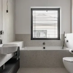 Nowoczesna łazienka z wanną, umywalką i toaletą, wykończona płytkami imitującymi lastryko, z oknem z żaluzjami i minimalistycznym oświetleniem.