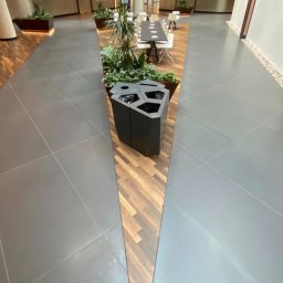 IWONA MAŁGORZATA CHMIELEWSKA PROFIT LINE - Wnętrze komercyjne z szarą podłogą z płytek, drewnianymi panelami w kształcie klina i roślinami w donicach, widok z góry.