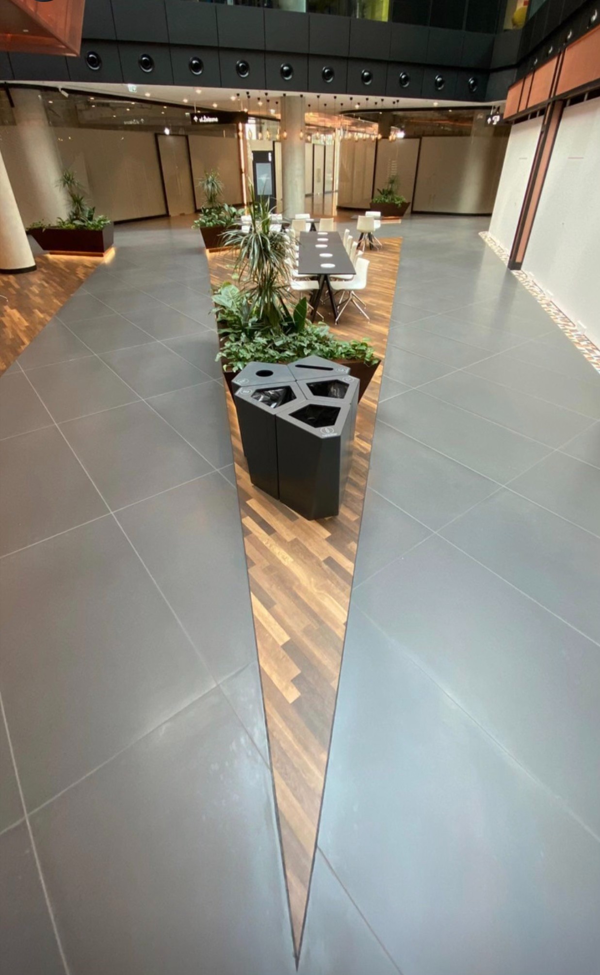 Wnętrze komercyjne z szarą podłogą z płytek, drewnianymi panelami w kształcie klina i roślinami w donicach, widok z góry.