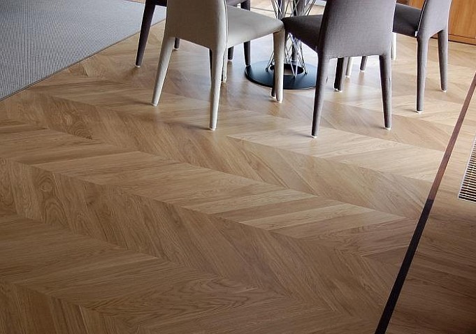 Parkiet ułożony we wzór jodełki francuskiej, widoczne krzesła i fragment stołu w tle, w rogu kratka wentylacyjna.