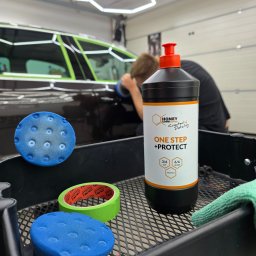 EMCARO Auto Detailing & Wrapping - Polerowanie auta pastą Honey Combination One Step + Protect. W tle auto z taśmą zabezpieczającą i polerka w użyciu. Na pierwszym planie akcesoria.
