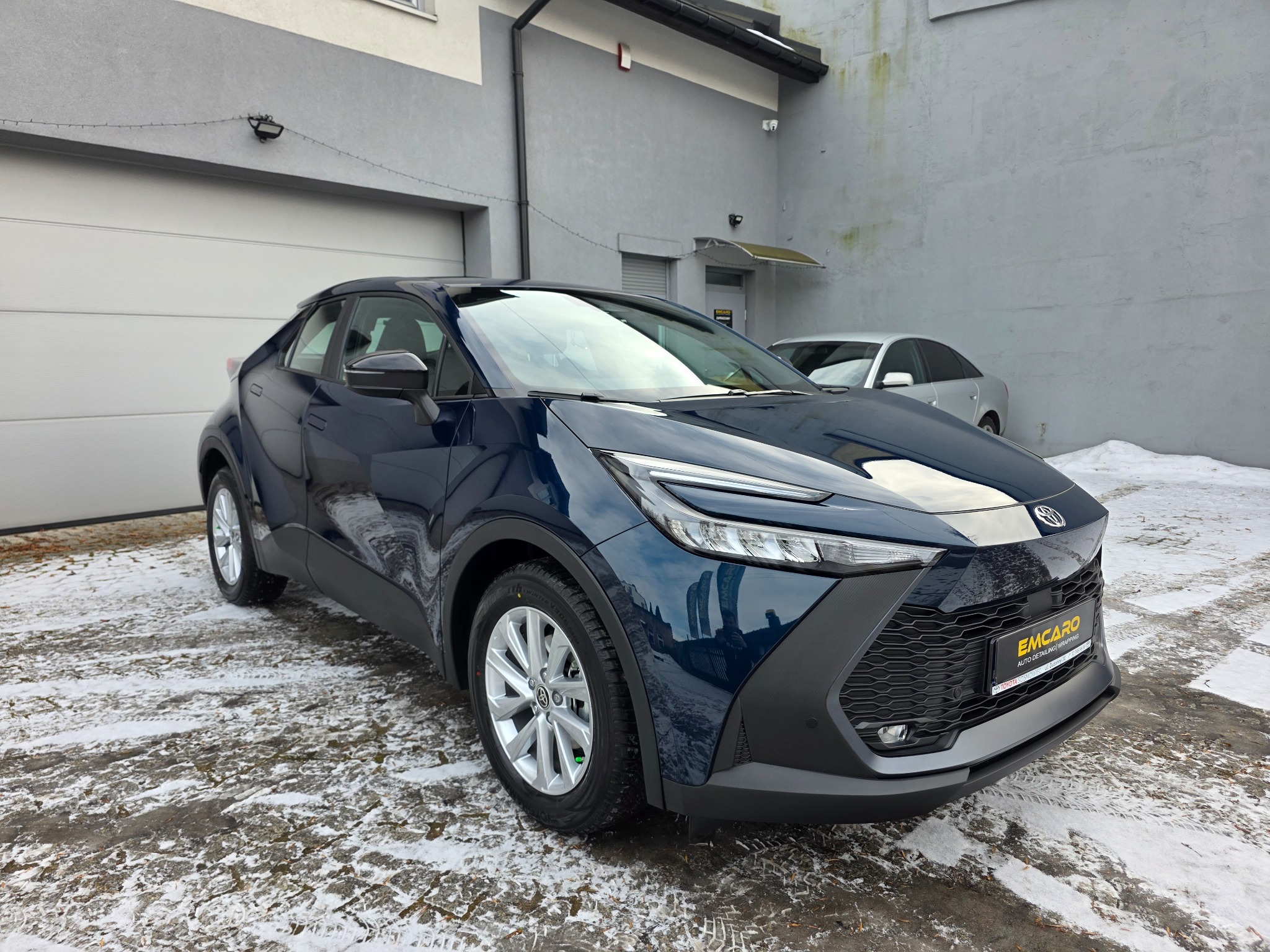Błyszczący, granatowy crossover na tle szarego budynku w Zawierciu. Widoczne detale: felgi, reflektory i logo firmy na grillu. Ślady śniegu na ziemi.
