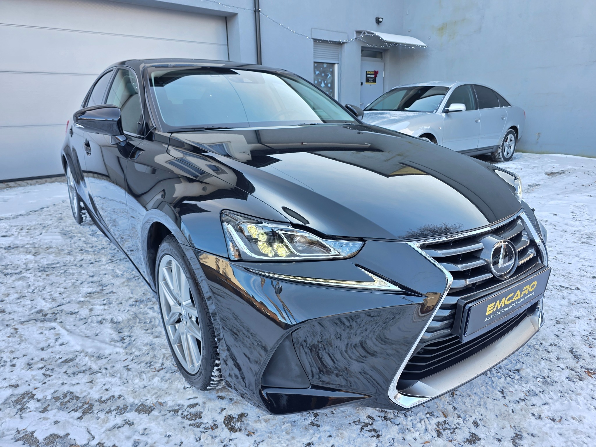Błyszczący, czarny Lexus IS po detailingu, zaparkowany na śniegu przed budynkiem. Widoczne logo firmy detailingowej na przednim zderzaku. Drugi samochód w tle.