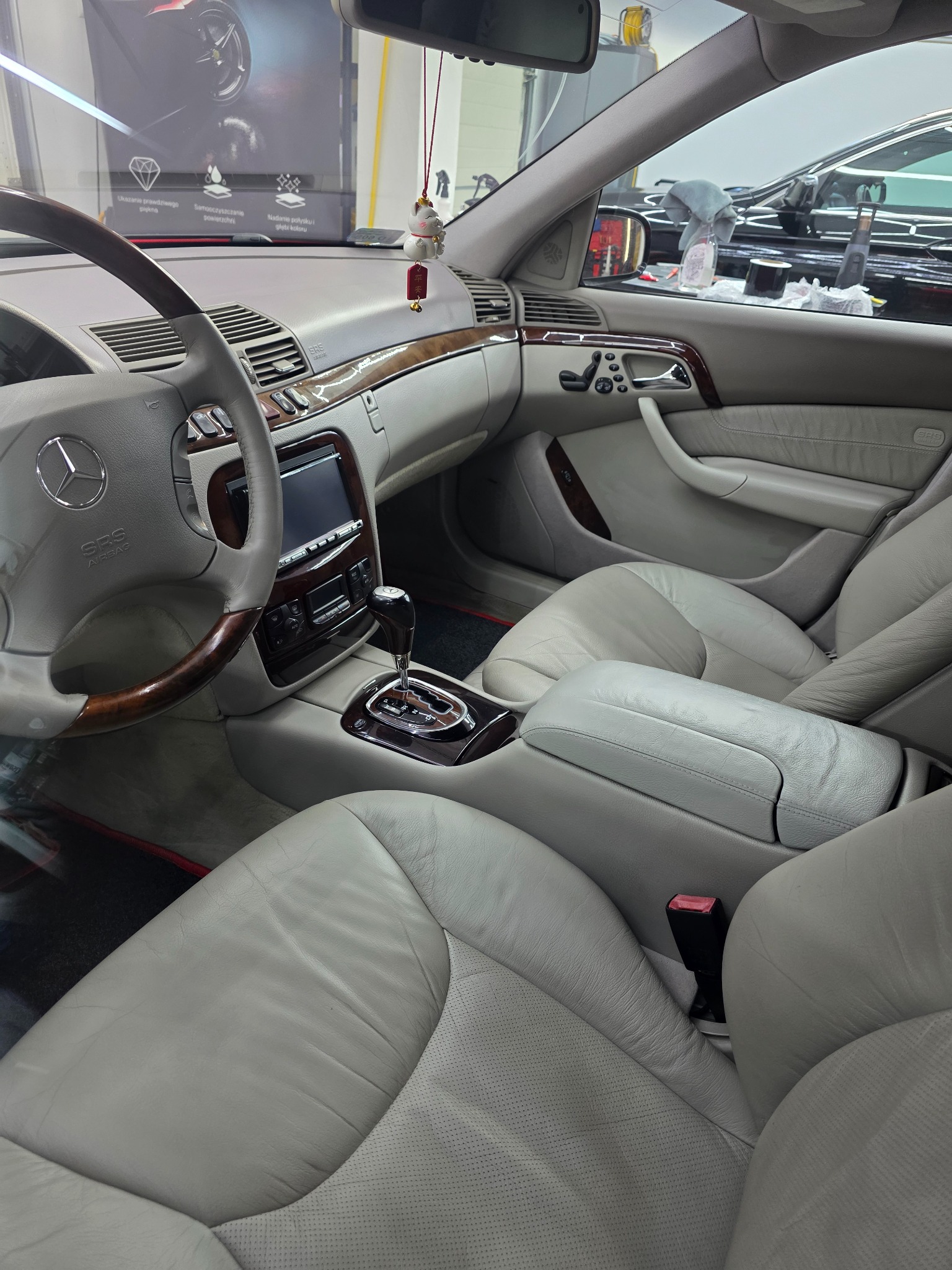 Wnętrze luksusowego Mercedesa po detailingu: jasna skórzana tapicerka, drewniane wykończenia, widoczny kokpit i fotele. Auto w trakcie czyszczenia w myjni.