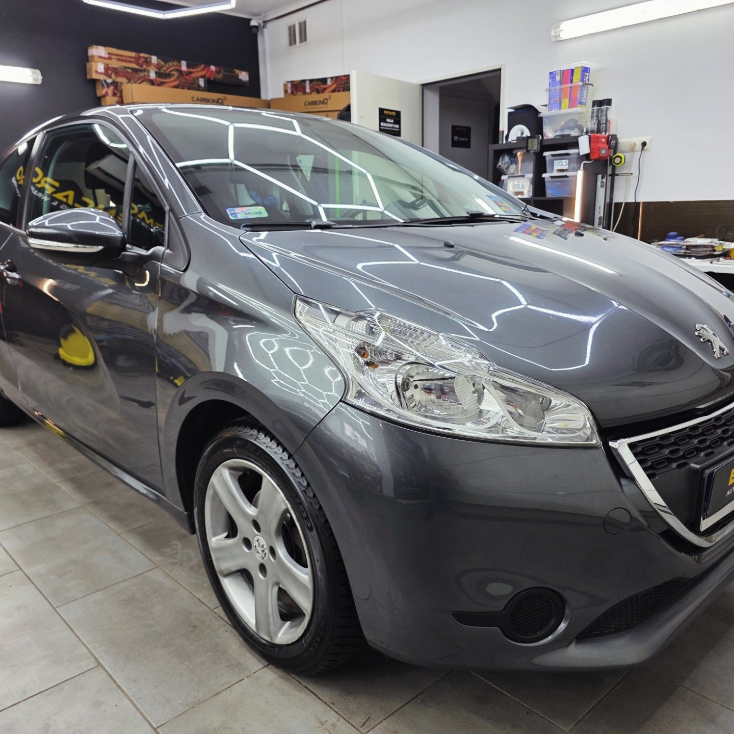 Błyszczący, szary Peugeot 208 po detailingu w myjni. Widoczne refleksy światła na karoserii, czyste felgi i zadbane wnętrze. Profesjonalne oświetlenie studia.