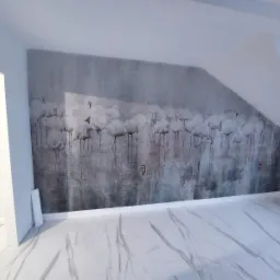 Wykończone wnętrze poddasza z fototapetą przedstawiającą stado flamingów na tle imitującym beton, biała marmurowa podłoga, listwy przypodłogowe.