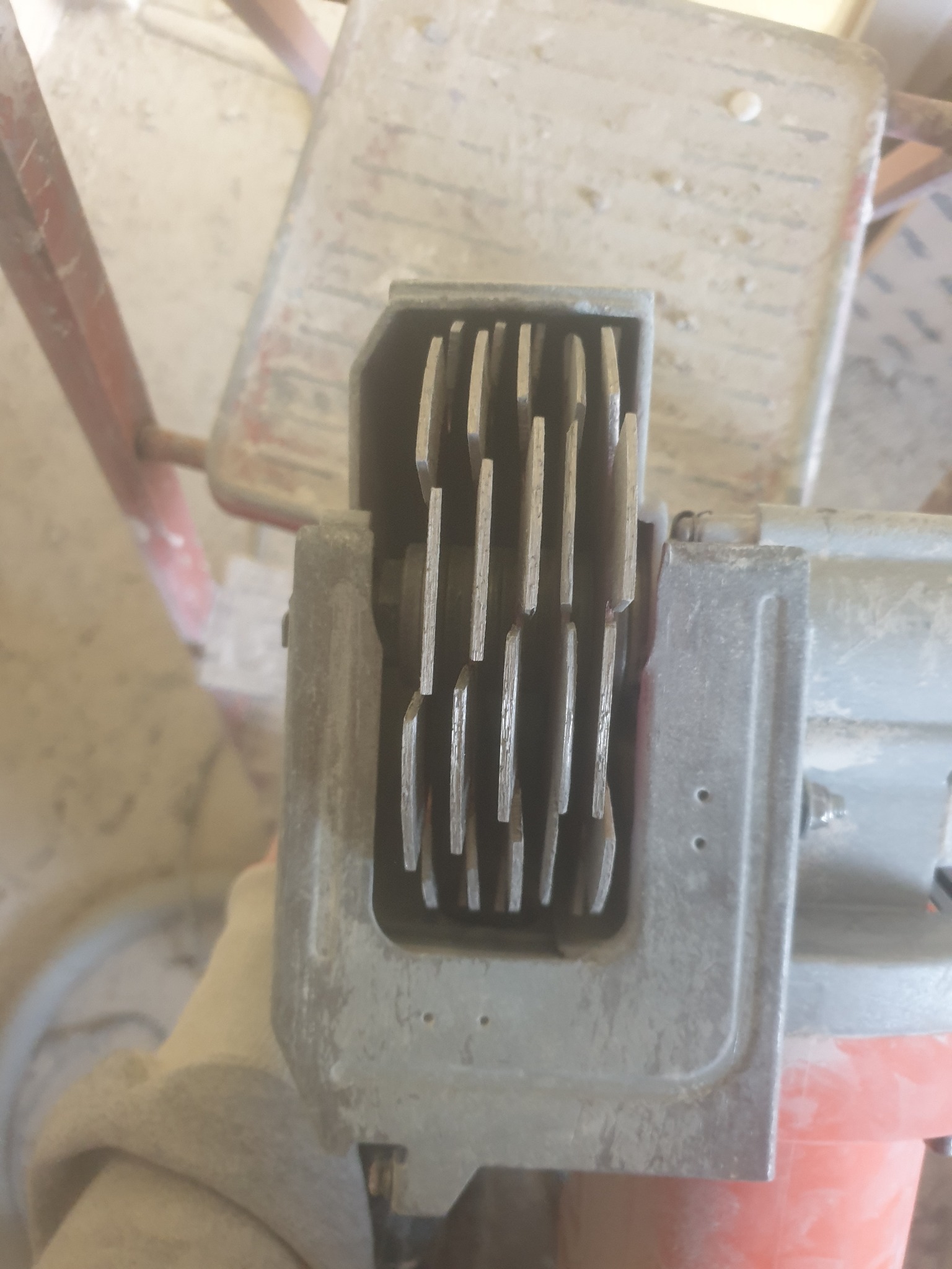 Szczegółowe ujęcie szczotkotrzymacza silnika elektrycznego z widocznymi lamelkami szczotek węglowych, mocno zabrudzonego pyłem.