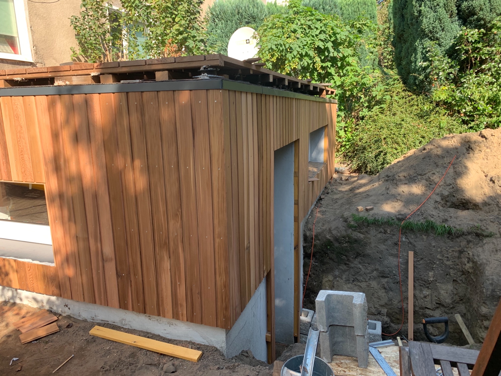 Nowa drewniana elewacja budynku w Pieszycach w trakcie montażu, widoczne okna, betonowa podstawa i wykop ziemny obok.