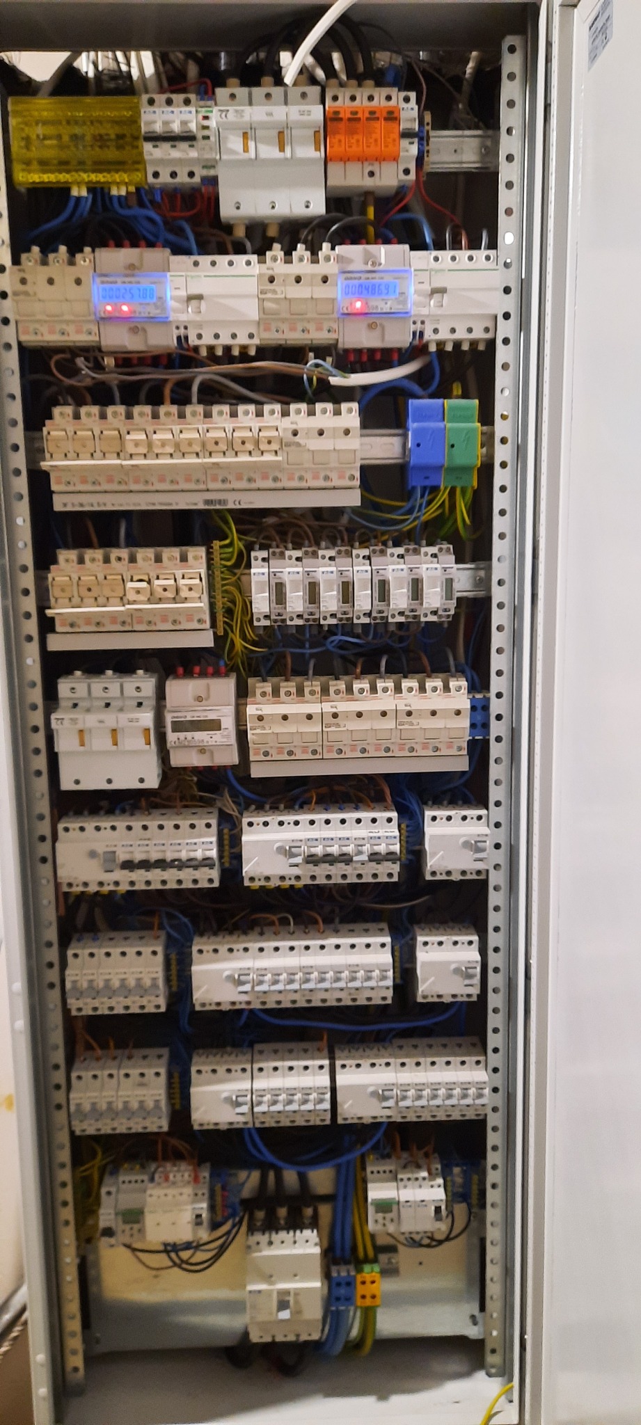 Rozdzielnica elektryczna z zainstalowanymi bezpiecznikami, licznikami energii i okablowaniem, widoczne różne kolory przewodów.