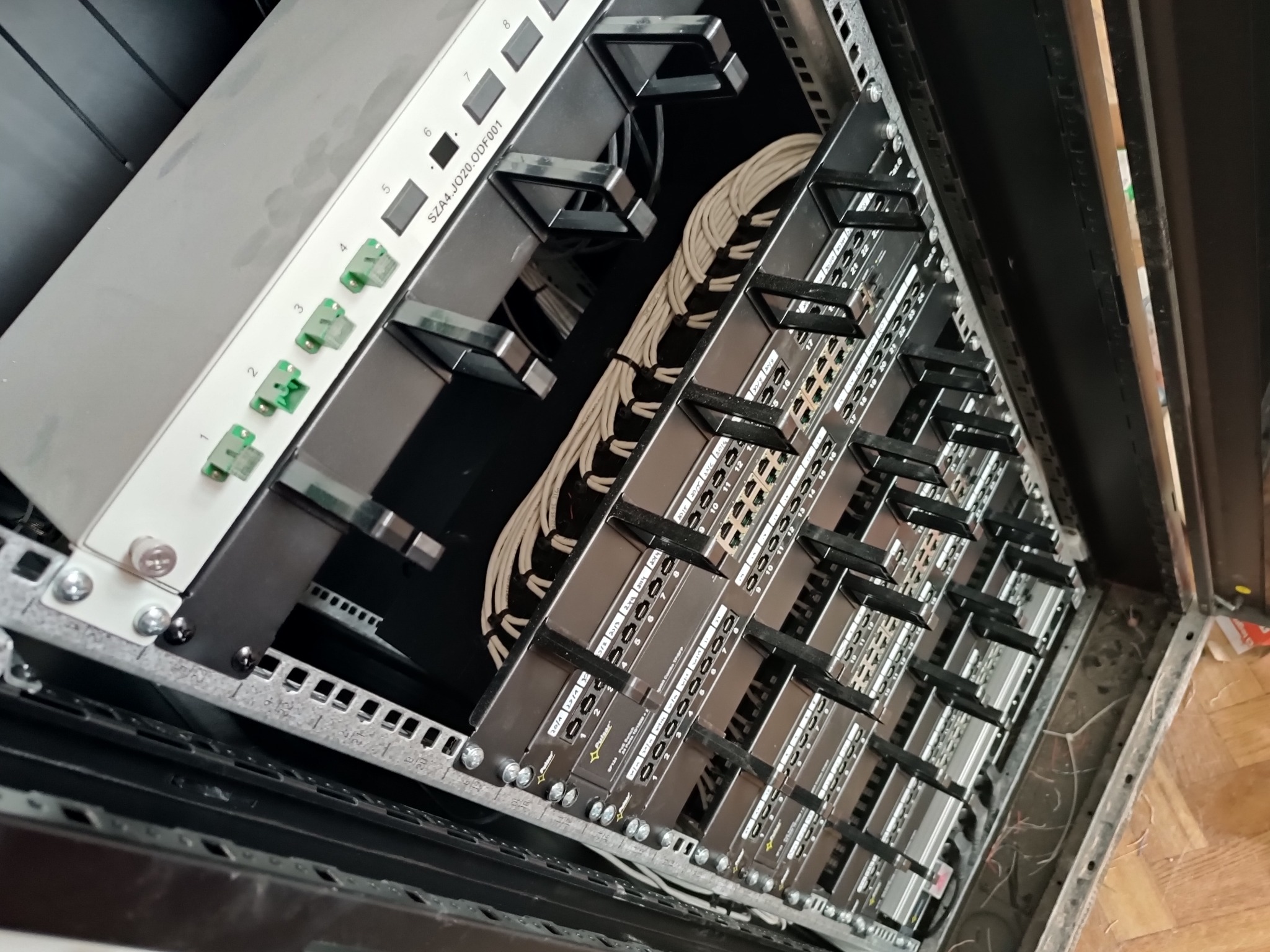 Panel krosowniczy w szafie rack z podłączonymi kablami światłowodowymi, widoczne numerowane porty i złącza.